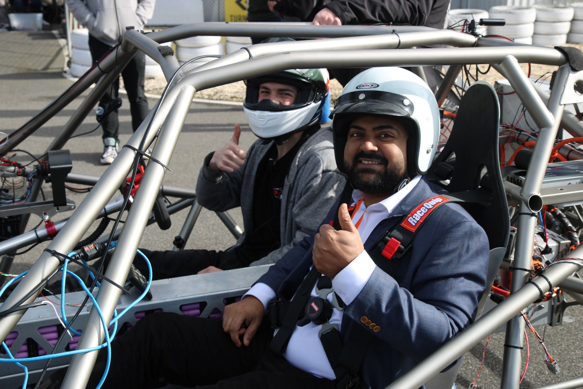 Alinta Energy employee sits in the chassis of the Deakin team Dust car. He is wearing a suit and crash helmet and giving a thumbs up gesture.