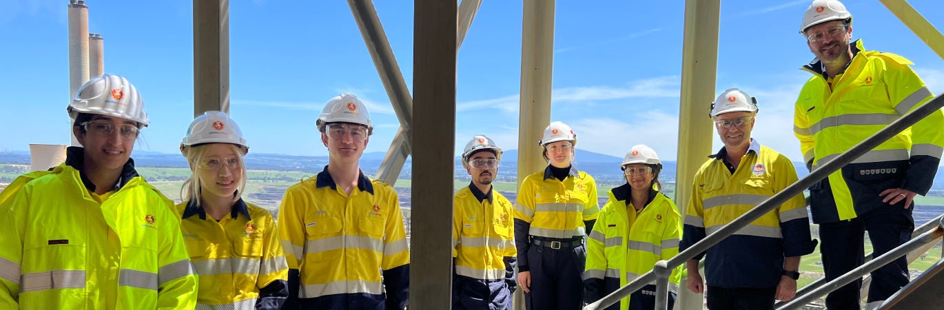 Line of young graduates and interns dressed in high visibility wear and hard hats on a set of stairs