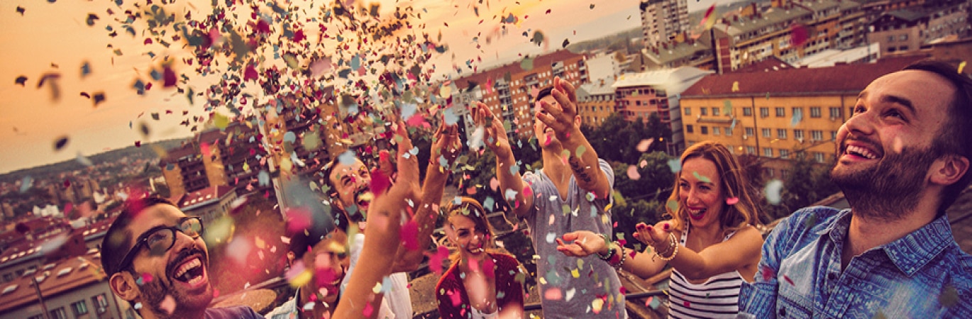 Group of smiling young people on a rooftop throwing confetti in the air in celebration