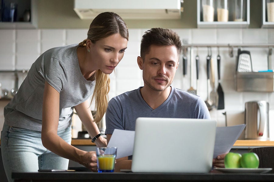 Serious young couple checking papers filling online form on website or holding documents searching information online using laptop banking internet application for calculating paying domestic bills