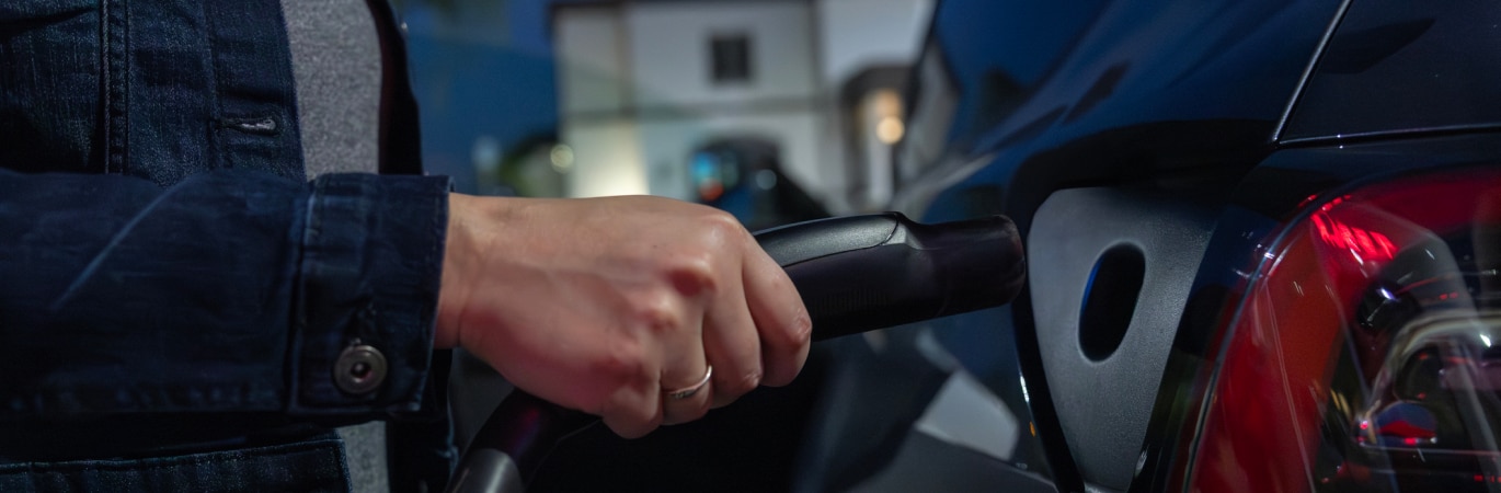 Close up of a woman's hand plugging in an EV charging lead outside her home at night