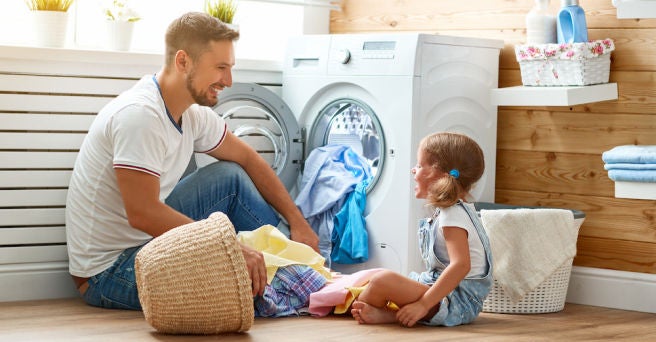 Father and daughter organising clothes into a washing machine