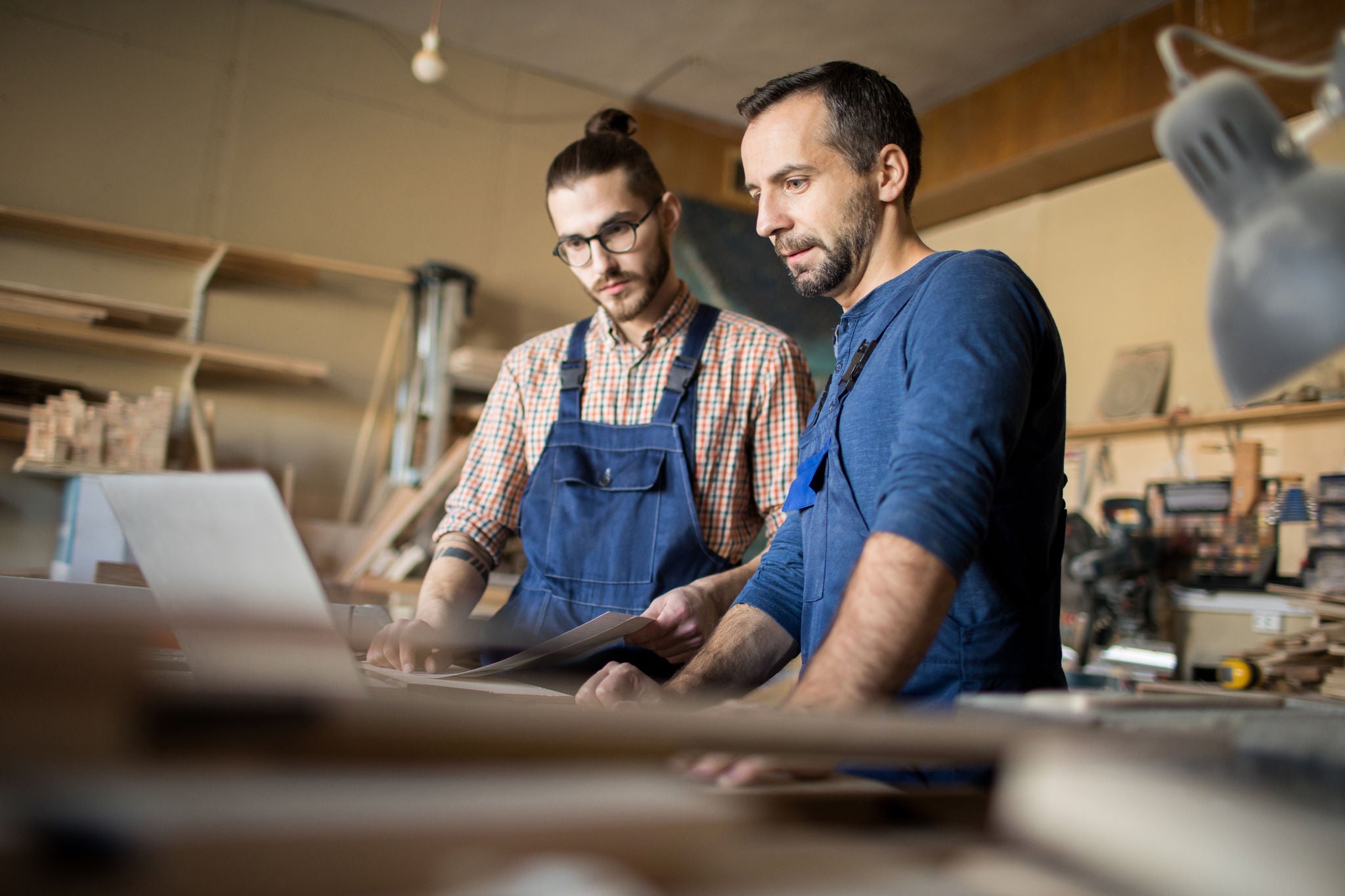 Low angle portrait of two modern artisans using laptop in workshop while working with wood together, copy space (Low angle portrait of two modern artisans using laptop in workshop while working with wood together, copy space, ASCII, 112 components, 11
