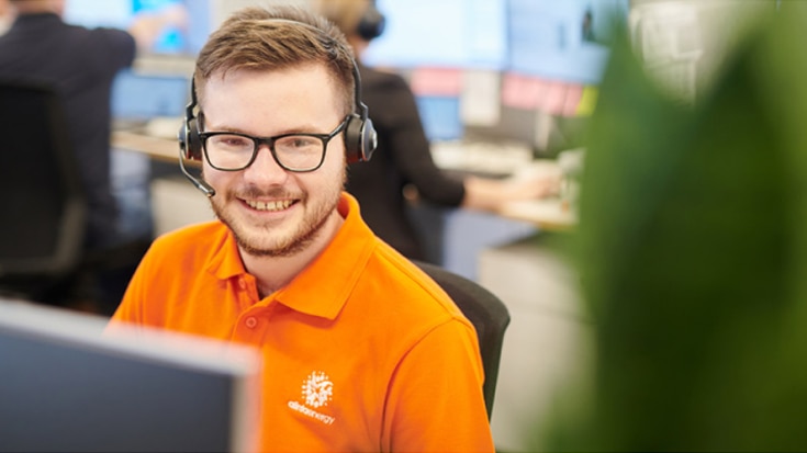 Smiling bearded customer service team member wearing a headset and looking at a computer monitor
