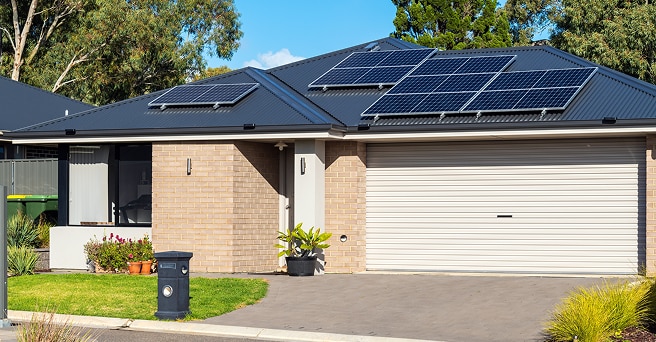 Australian house in the suburbs with many solar panels on the roof against a blue sky