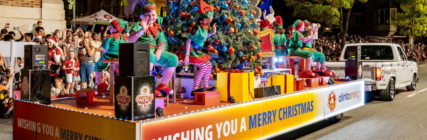 Brightly coloured Christmas Pageant float with children dressed as elves waving to the crowd