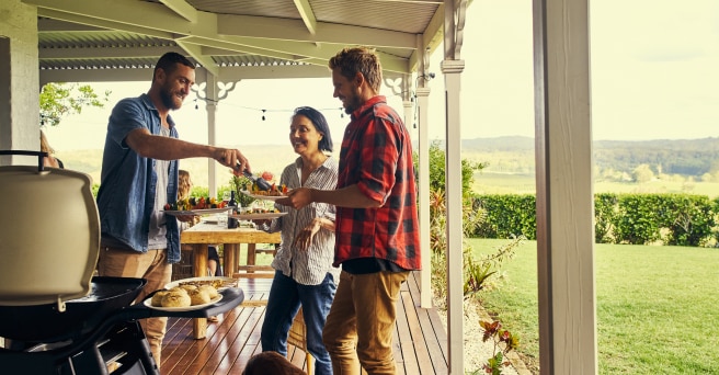 Man smiling as he serves BBQ food on verandah