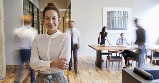 Woman with arms folded smiling in busy office