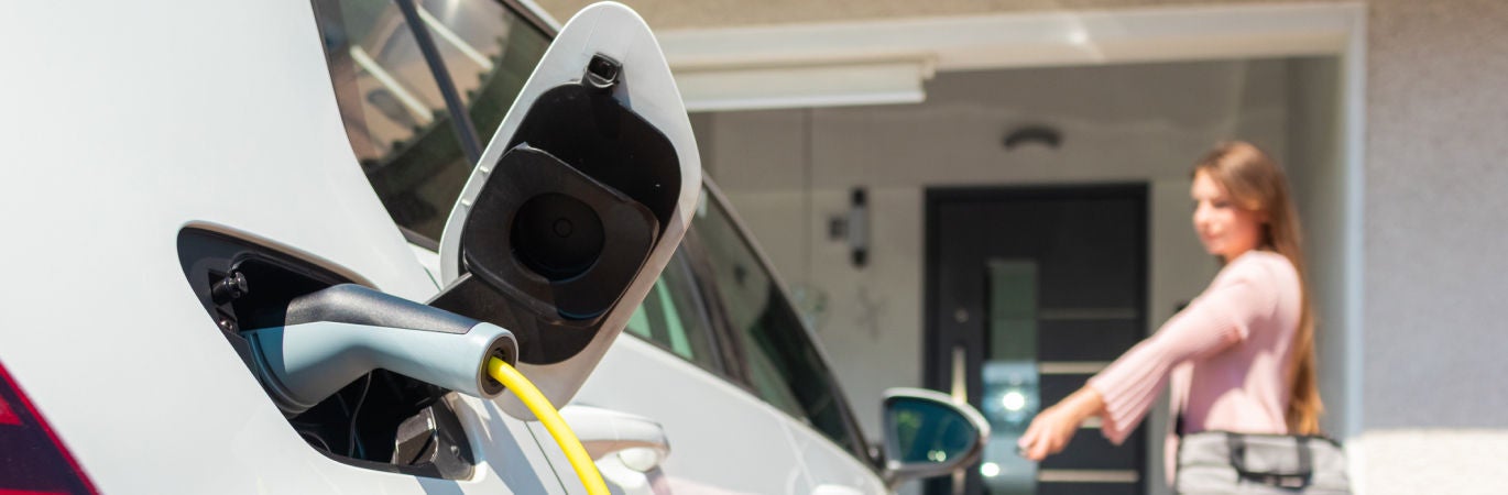 Close up of EV charger plugged into white car with owner in the background locking the car