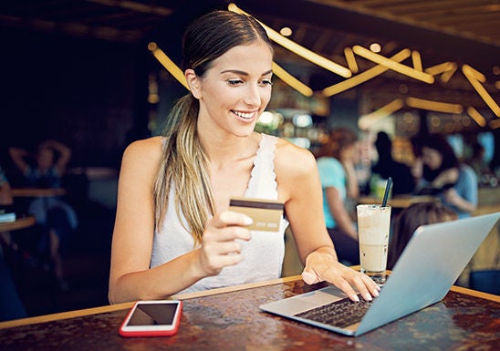 Woman on her laptop, holding a credit card and smiling, in a bar