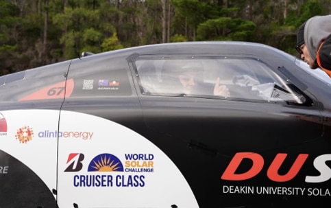 A close-up of the side of the Dust car showing its right side door and window. A driver sits inside with a helmet making a thumbs up gesture.