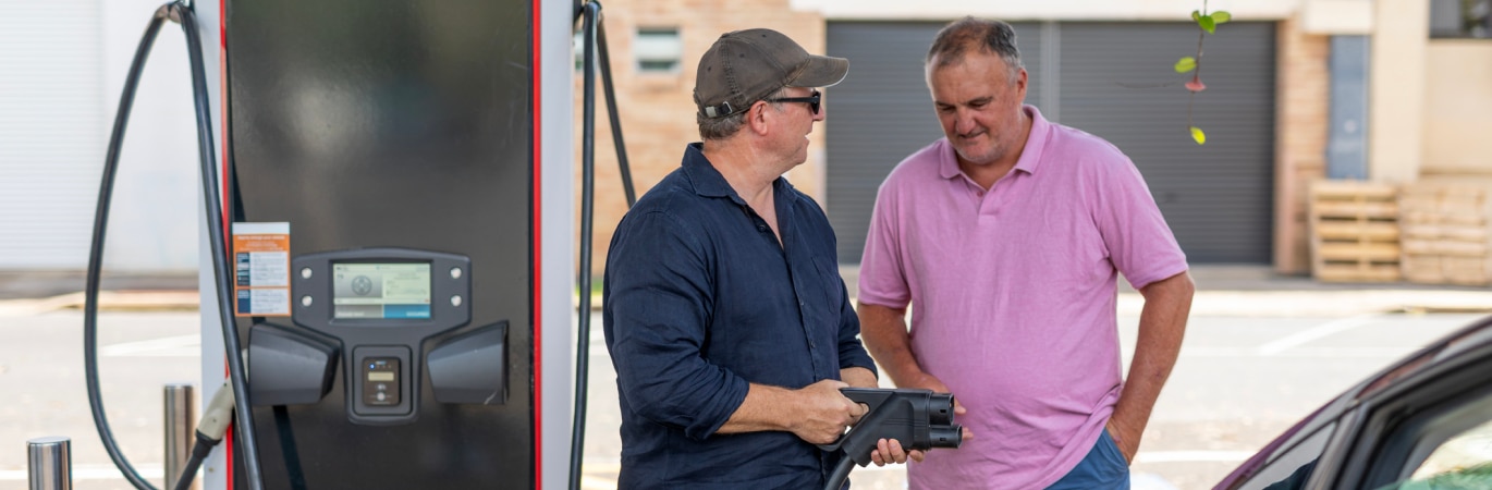 Two men standing by the side of an EV charger and having a discussion