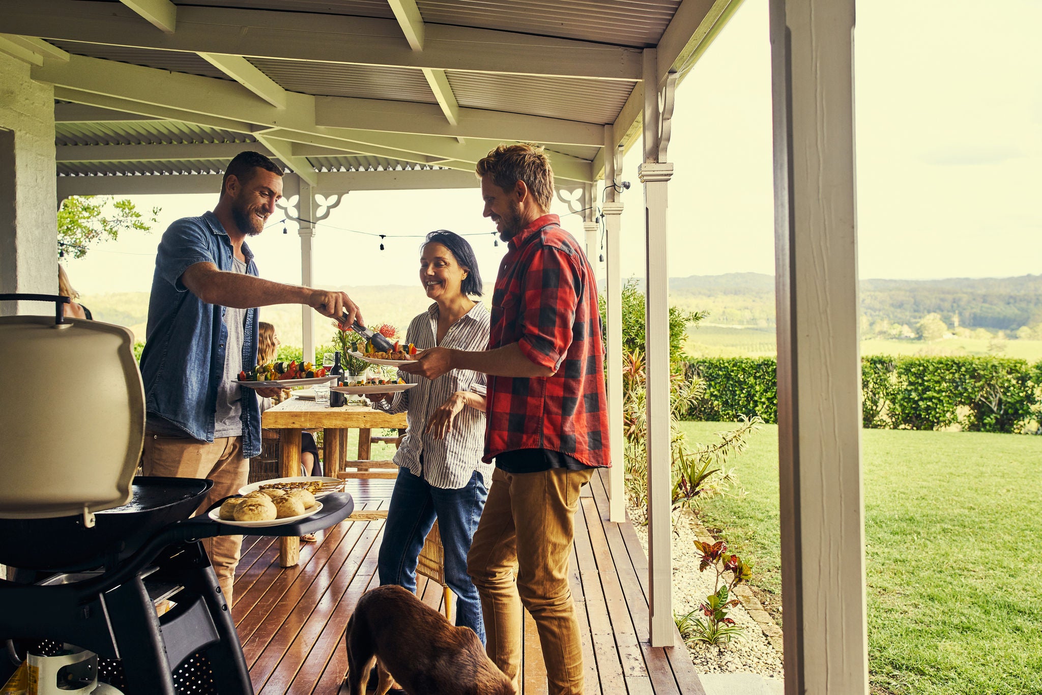 Man serving people food from a BBQ on an outside verandah
