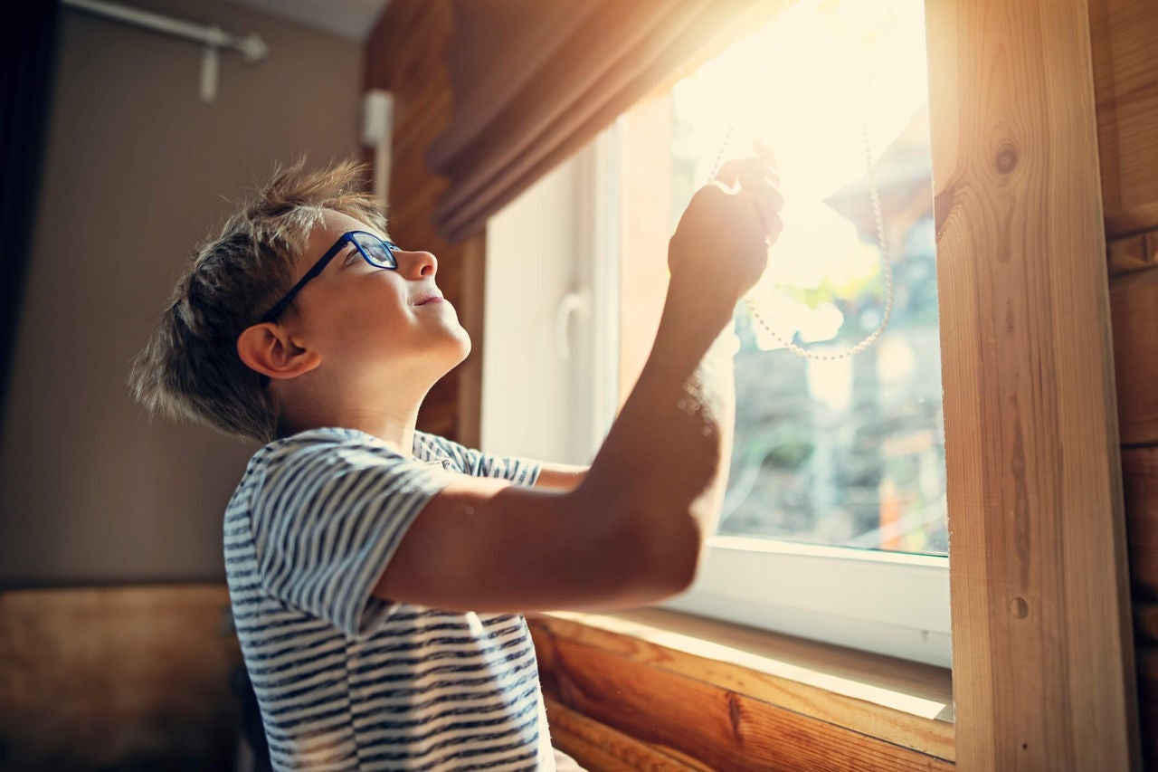 Boy pulling up window blind to let in the sunshine