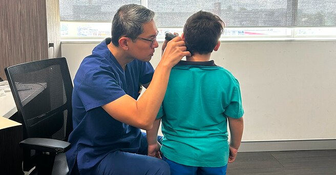 In a medical office, a doctor examines a young boy's ear using an otoscope