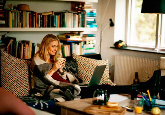 Woman on sofa wearing blanket and drinking hot drink