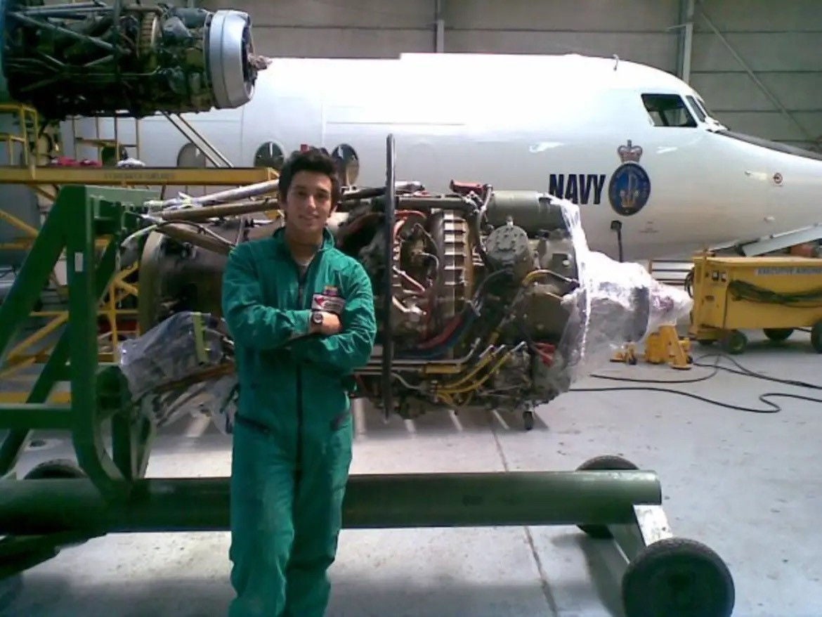 An image of Mario in green overalls, standing in front of a plane turbine with his arms crossed.