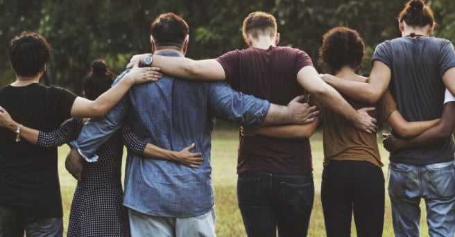 Group of six people from behind with arms around each other walking away from the camera