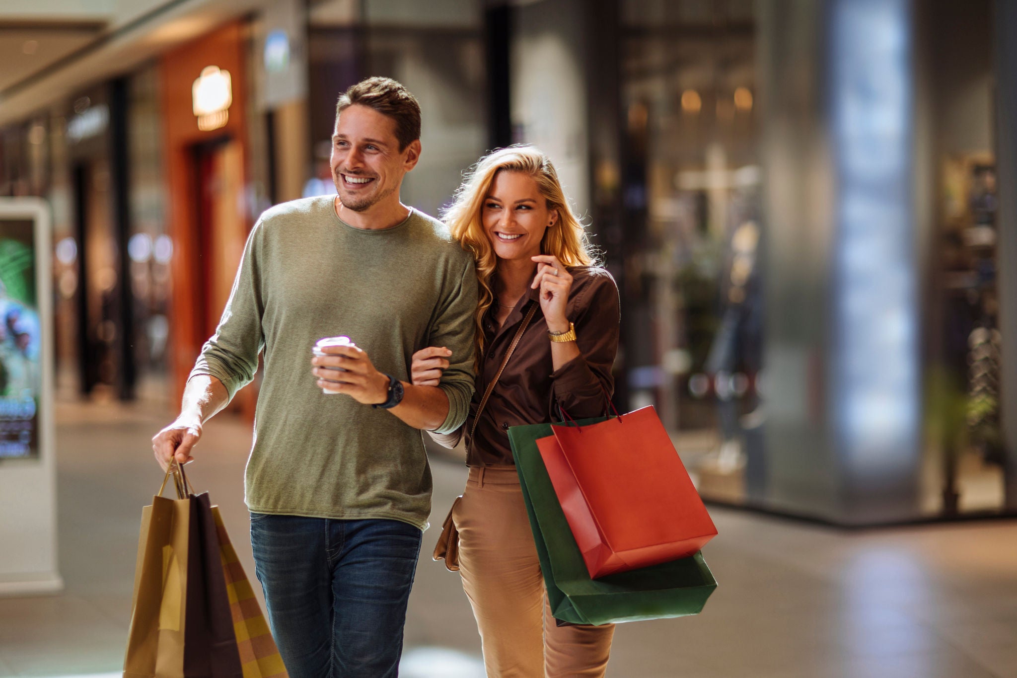 Laughing young couple walking through a mall holding shopping bags and a takeaway coffee