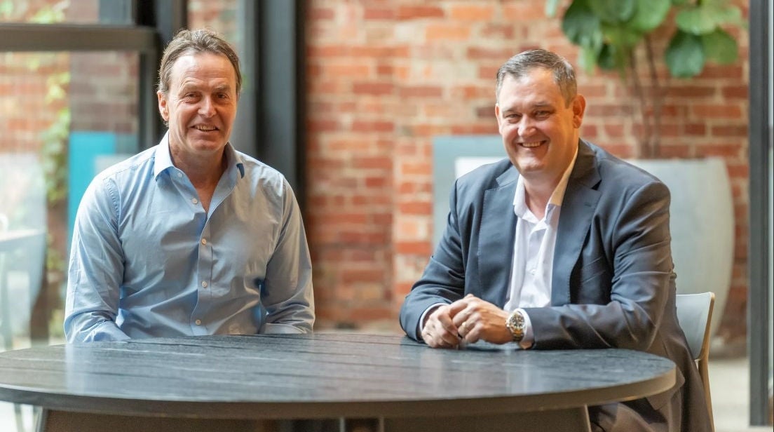 Tally CEO Andrew Duncan and Alinta Energy CEO & MD Jeff Dimery sit at a table smiling. Andrew is on the left and Jeff is on the right.