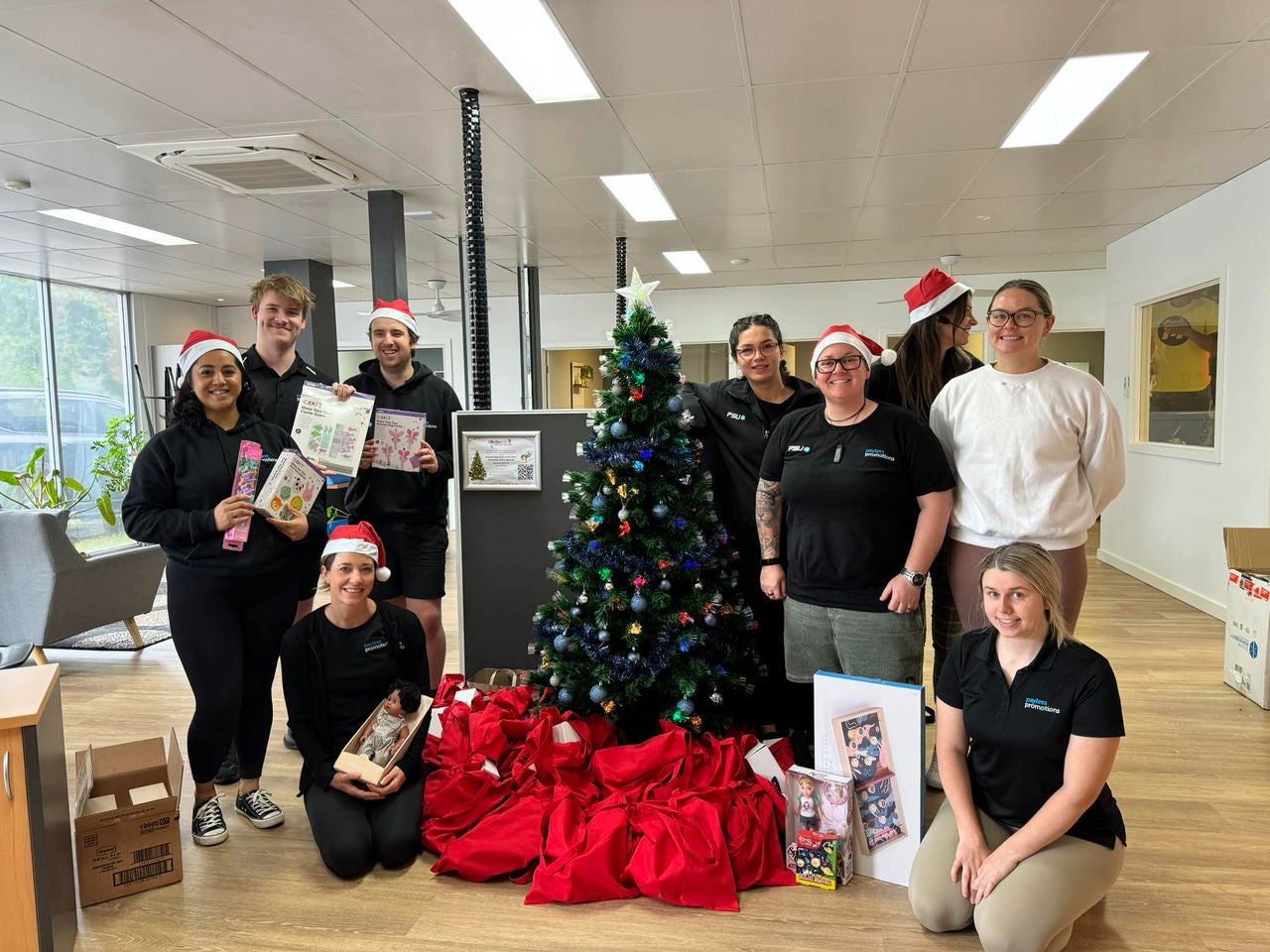 Volunteers from A Better Life For Foster Kids wearing Santa hats and grouped around a Christmas tree