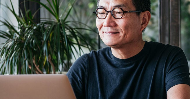 Smiling mature man in glasses on a laptop with a large plant behind him