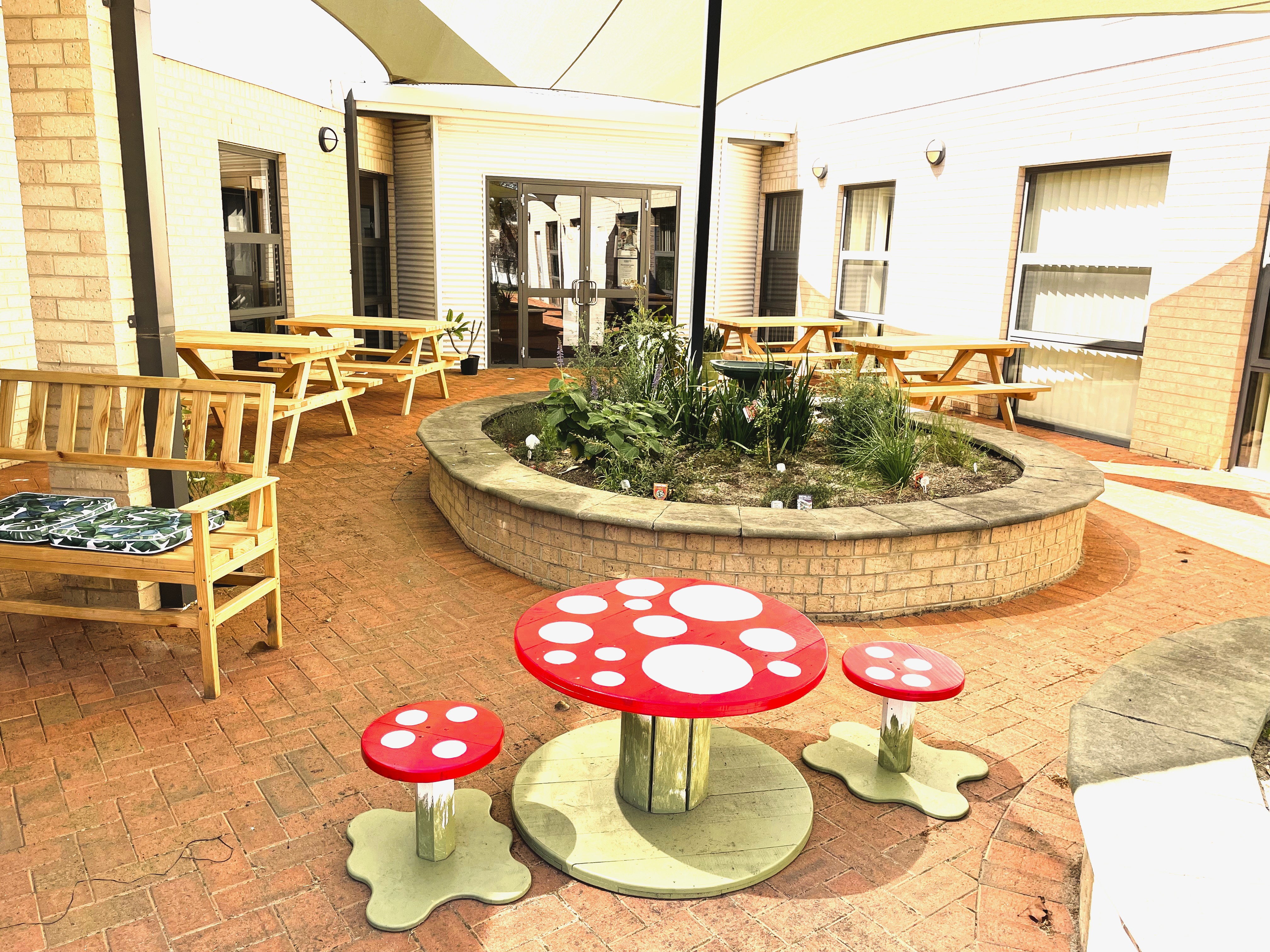 An image of the completed garden at Waroona CRC, with red-and-white, toadstool-themed table and stools pictured in the foreground.