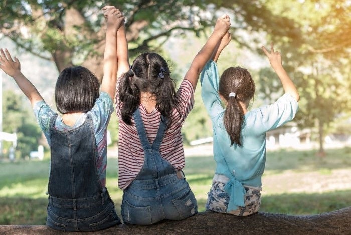 Three girls sitting on a tree branch holding hands in air