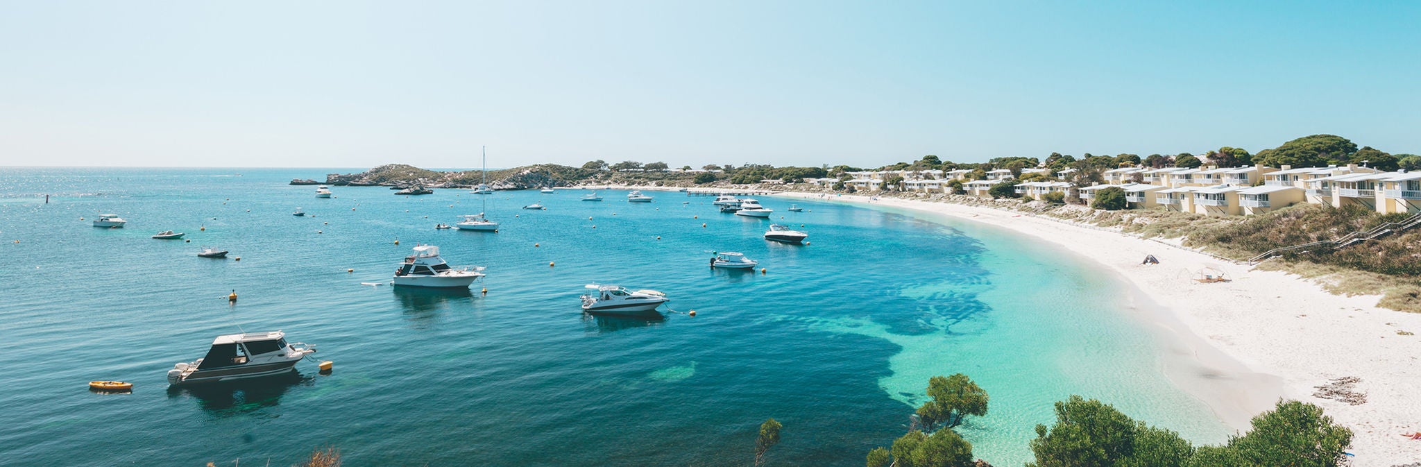 Overlooking a bay in Rottnest Island showing turquoise sea, boats and chalets on the dunes