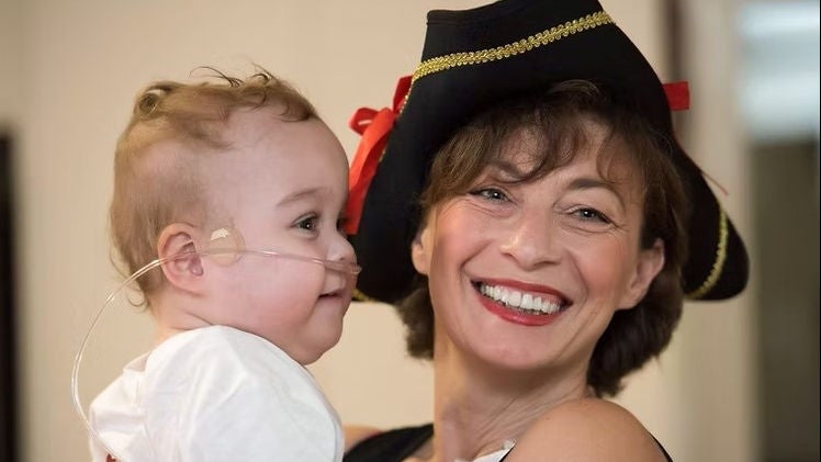A close up of a smiling woman in a festive hat holding a baby with a cannula.