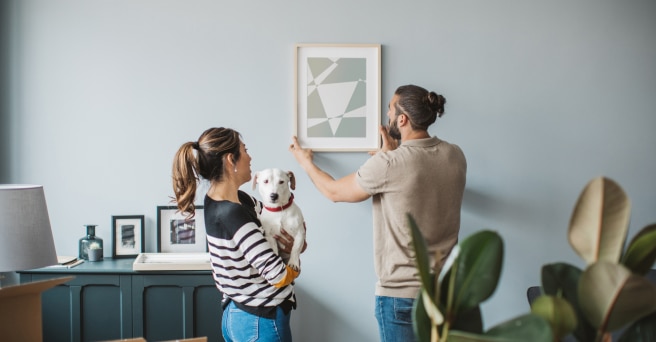 Couple with dog hanging picture on wall