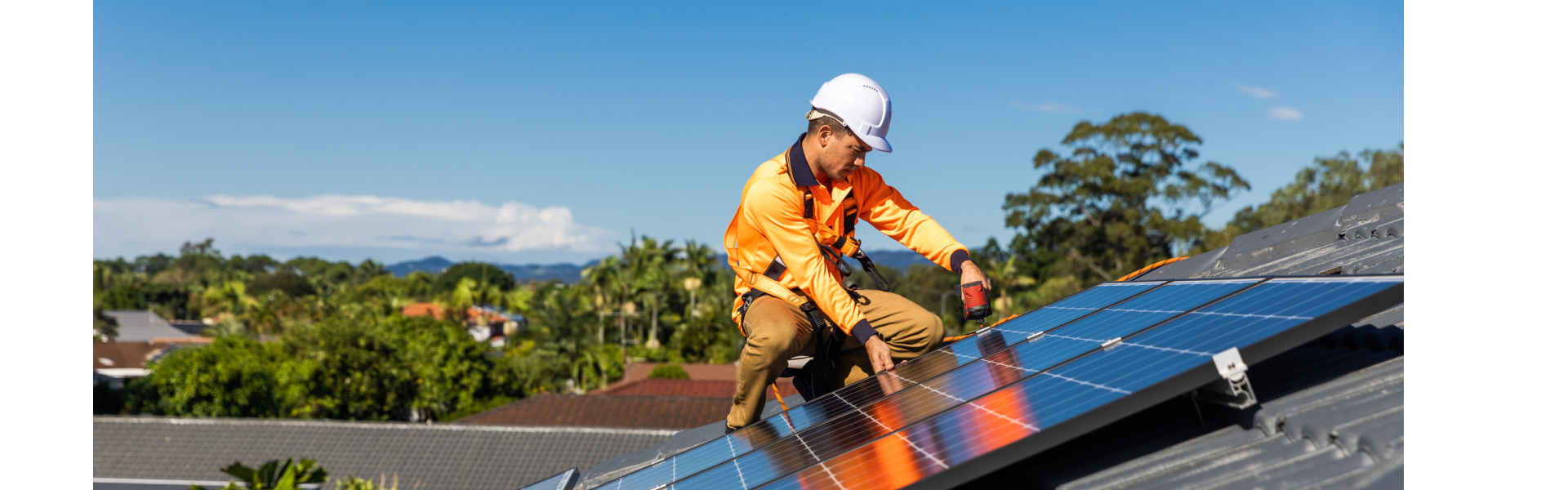 Solar installer in high visibility workwear and hard hat kneeling on a roof and fitting solar panels