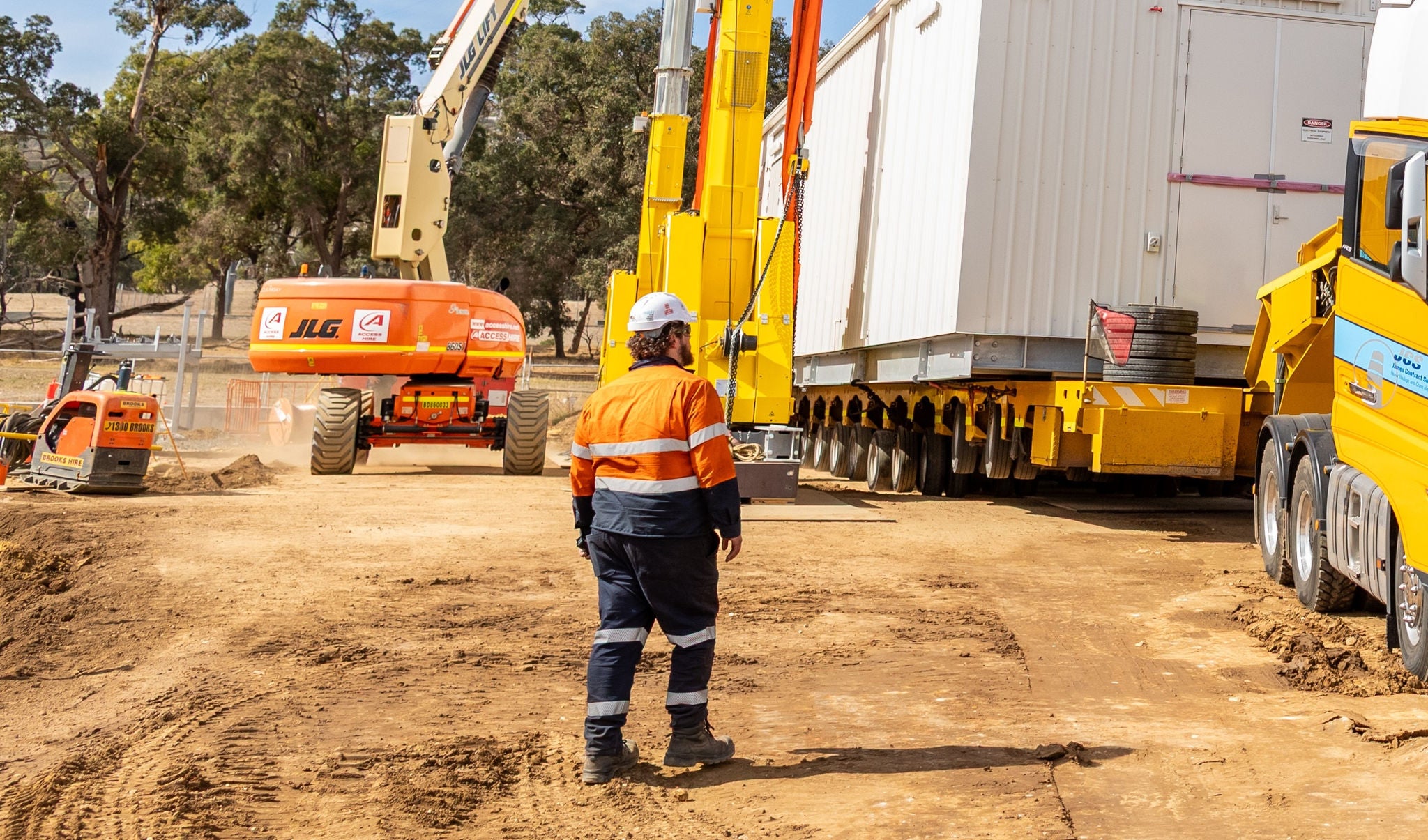A worker in hard hat and orange hi-vis vest stands net to a truck onsite.
