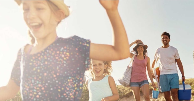 Close up of laughing girl in the sun followed by family heading down to the beach with an esky of food