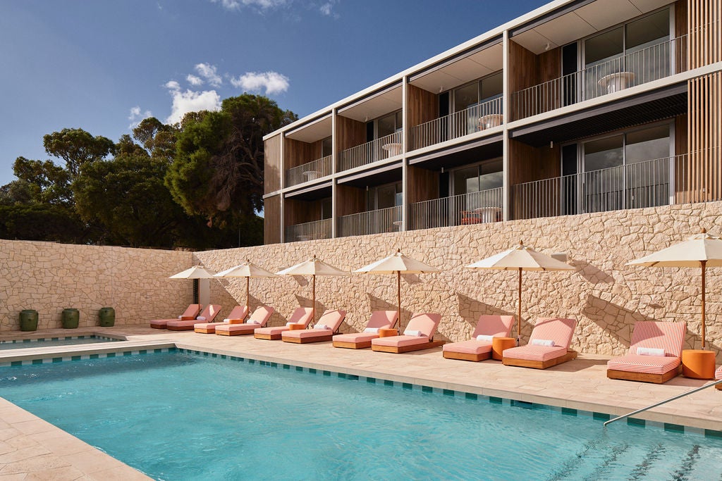 Pool view exterior of the The Lodge at Rottnest Island featuring peach coloured sun loungers by a pool