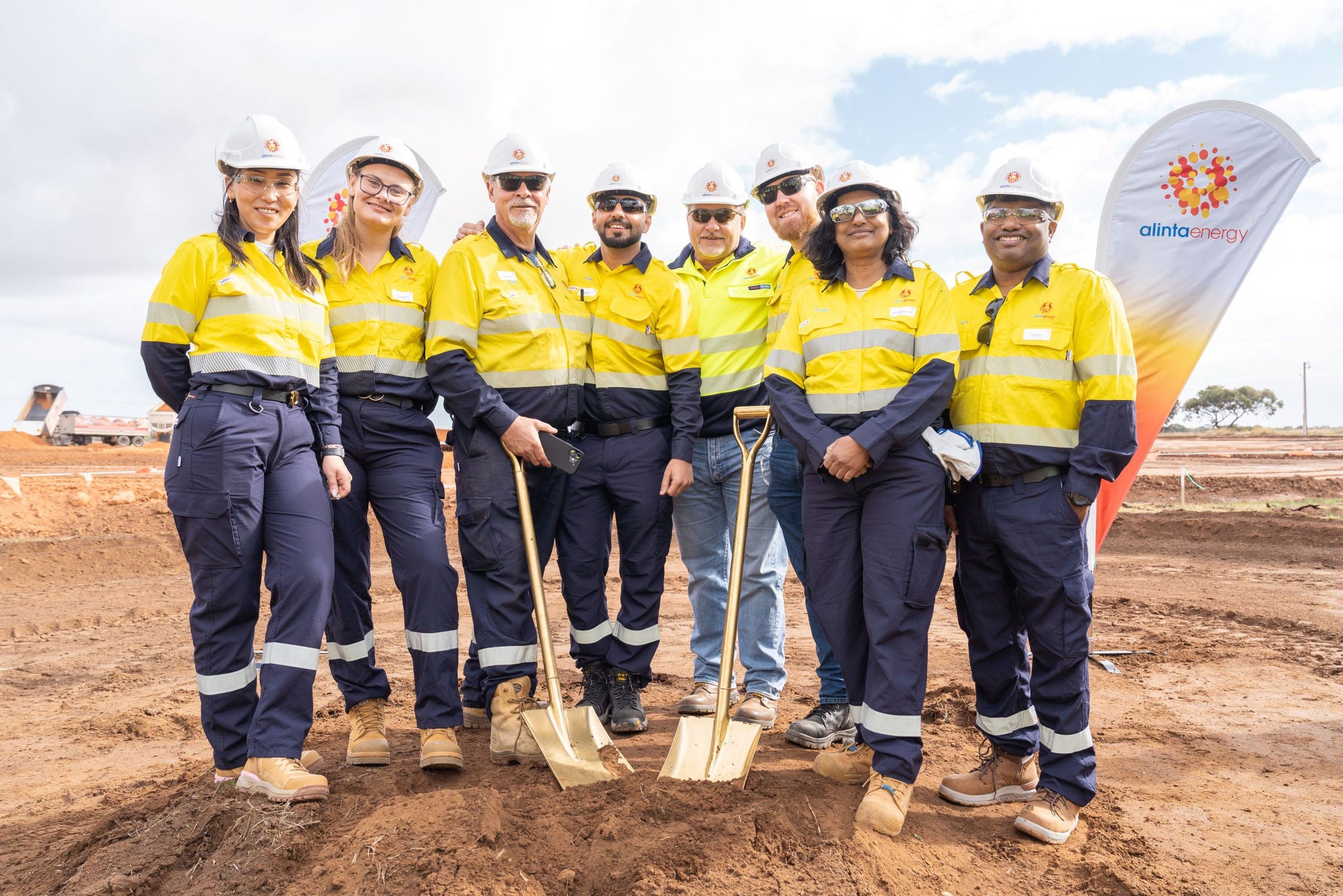 The Reeves Plains Energy Hub Alinta Energy team pose for a photo at the sod turn ceremony marking the start of construction. They are all wearing hard hats and yellow hi-vis gear. Two of them hold shovels.