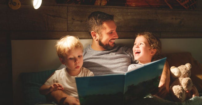 Smiling father reading story book to two kids in bed