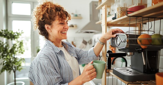 Smiling woman in a bright airy kitchen making a cup of coffee using her coffee machine