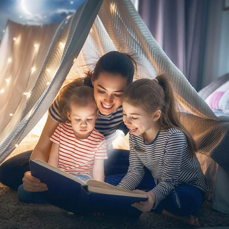 Mum reading a story to daughters by torchlight.