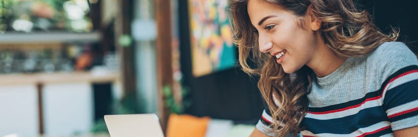 Women in striped t shirt smiling at her laptop screen in a colourful location