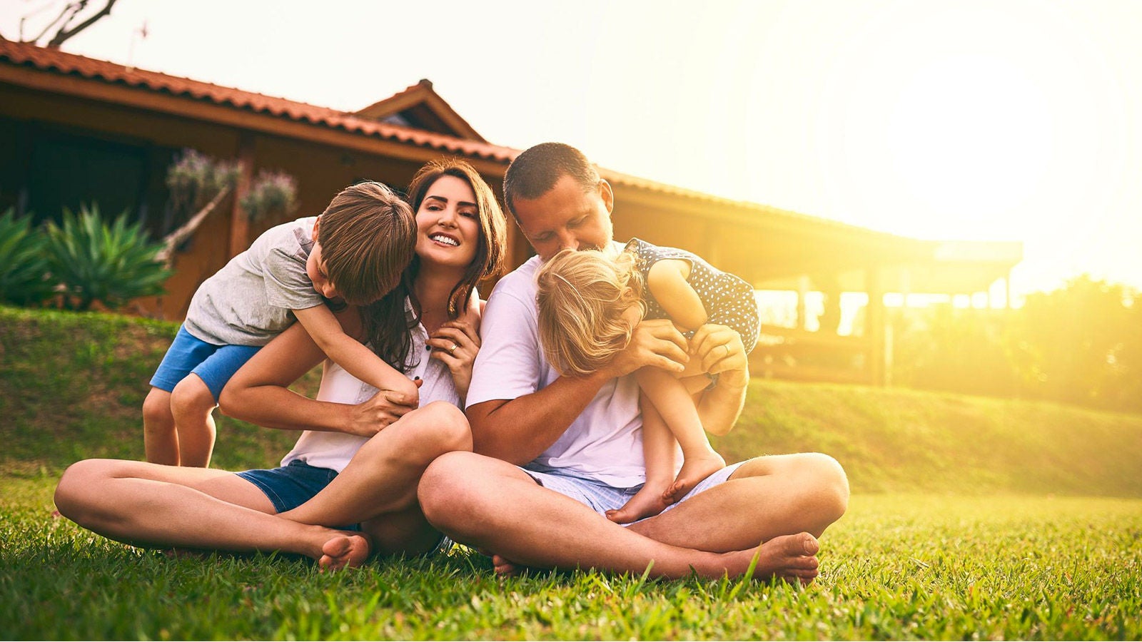 Family playing outside in sun hugging kids