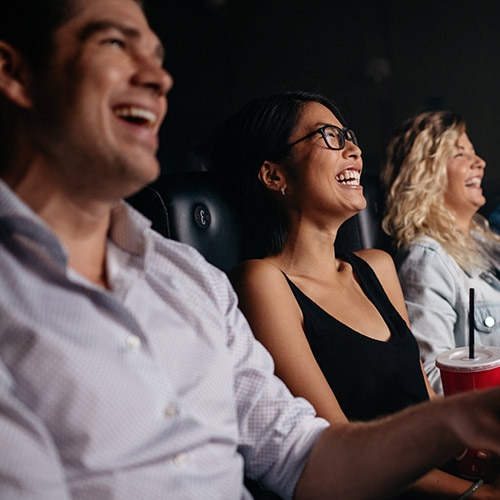 Three seated people laughing at a movie screening.