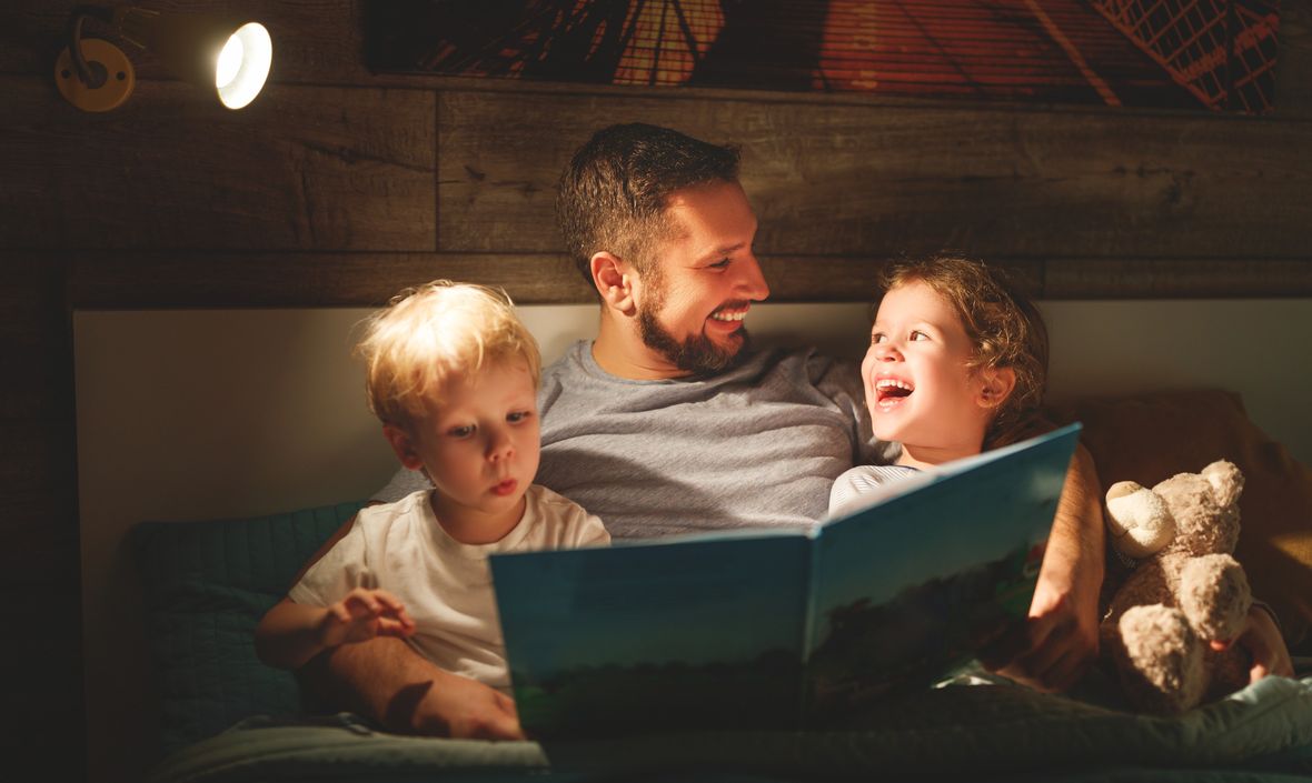 A father reading to 2 young children in bed.